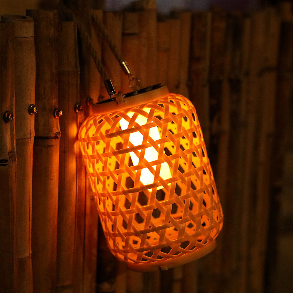 Rattan solar lantern hanging from a tree branch in a lush cottage garden