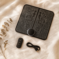 EMS foot massager mat with wireless remote, USB charging cable and dried eucalyptus arranged on cream linen fabric.